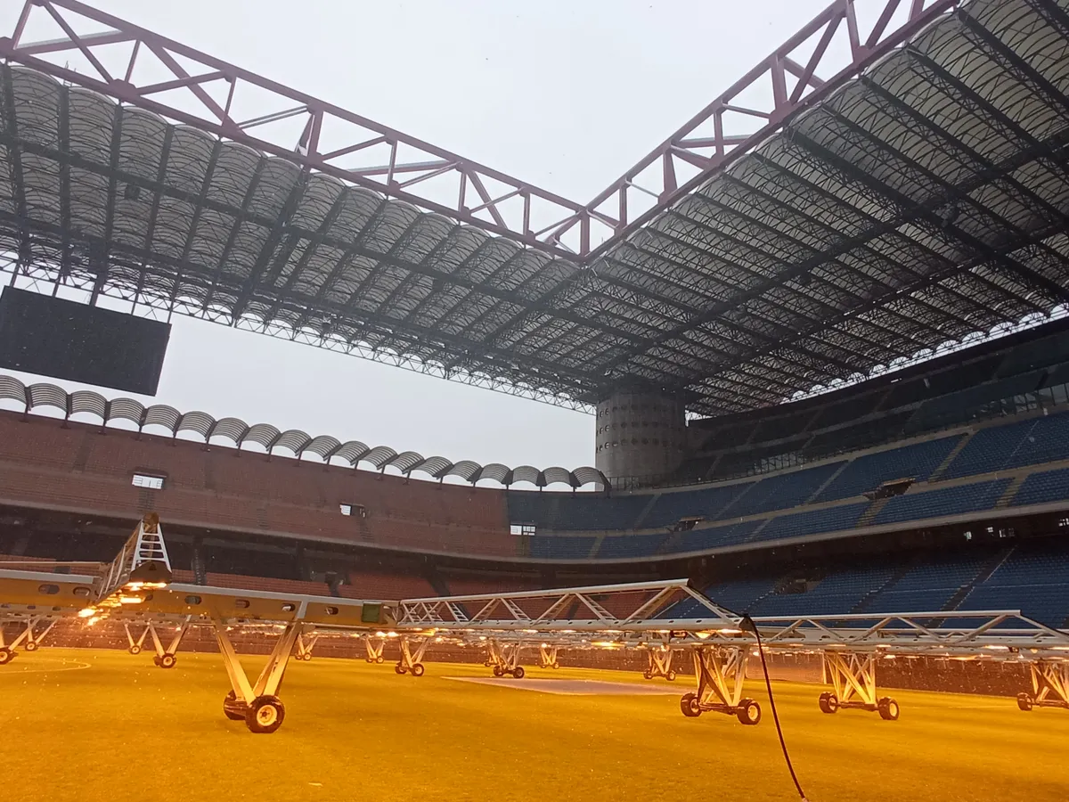 The empty San Siro bowl seen from pitch level on a San Siro stadium tour in Milan, red roof girders overhead