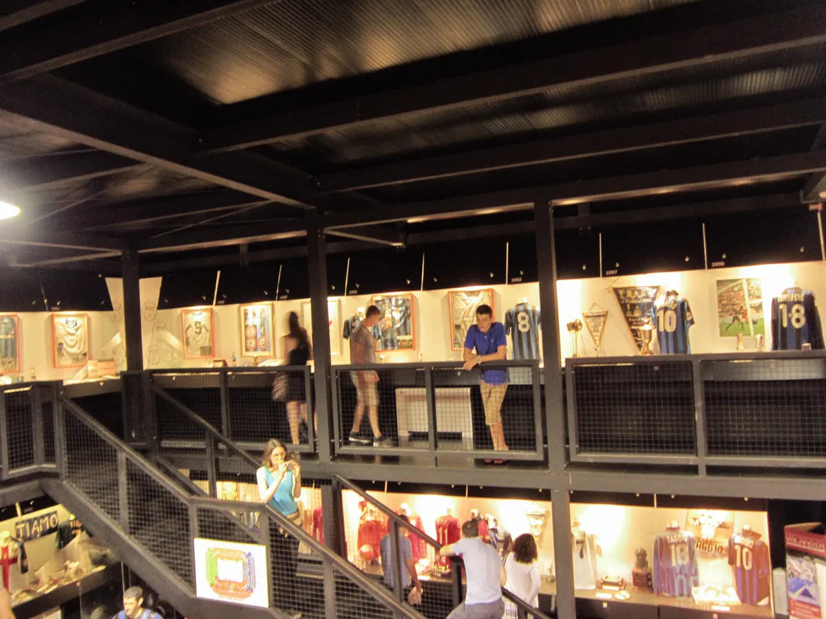 Visitors browsing shirt and trophy displays on the upper gallery of the San Siro museum in Milan, the indoor stop that makes the time slot matter more than the season